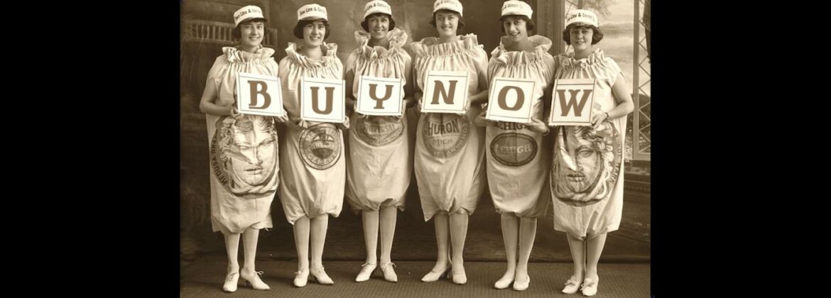 Girls in cement bags holding signs that spell out "Buy Now"